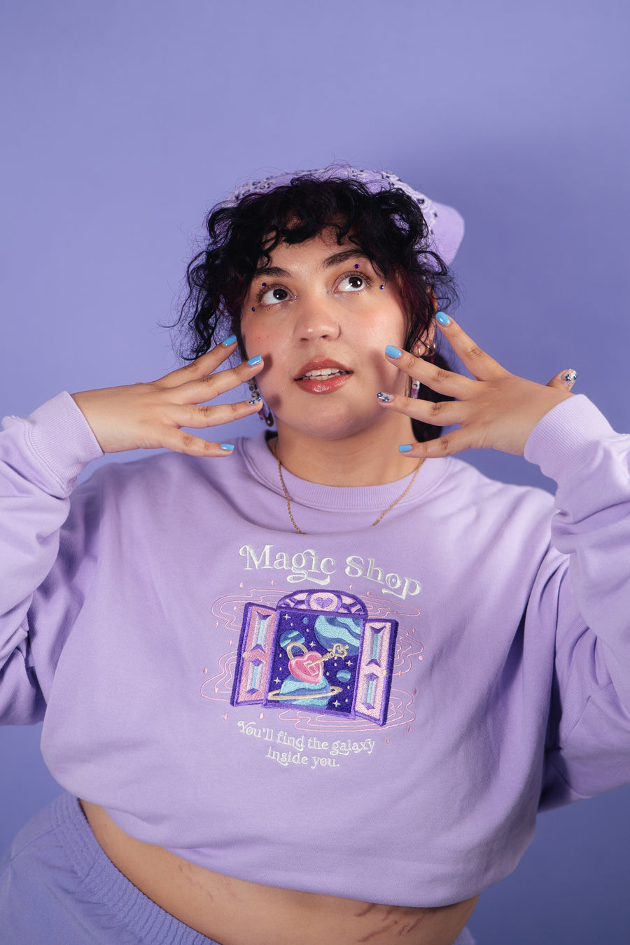 Model infront of purple wall wearing a purple crewneck sweatshirt inspired by the BTS song Magic Shop.
