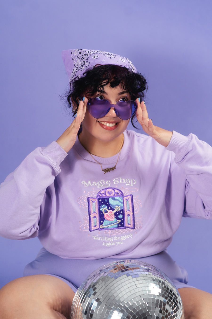 Model infront of purple wall wearing a purple crewneck sweatshirt inspired by the BTS song Magic Shop.